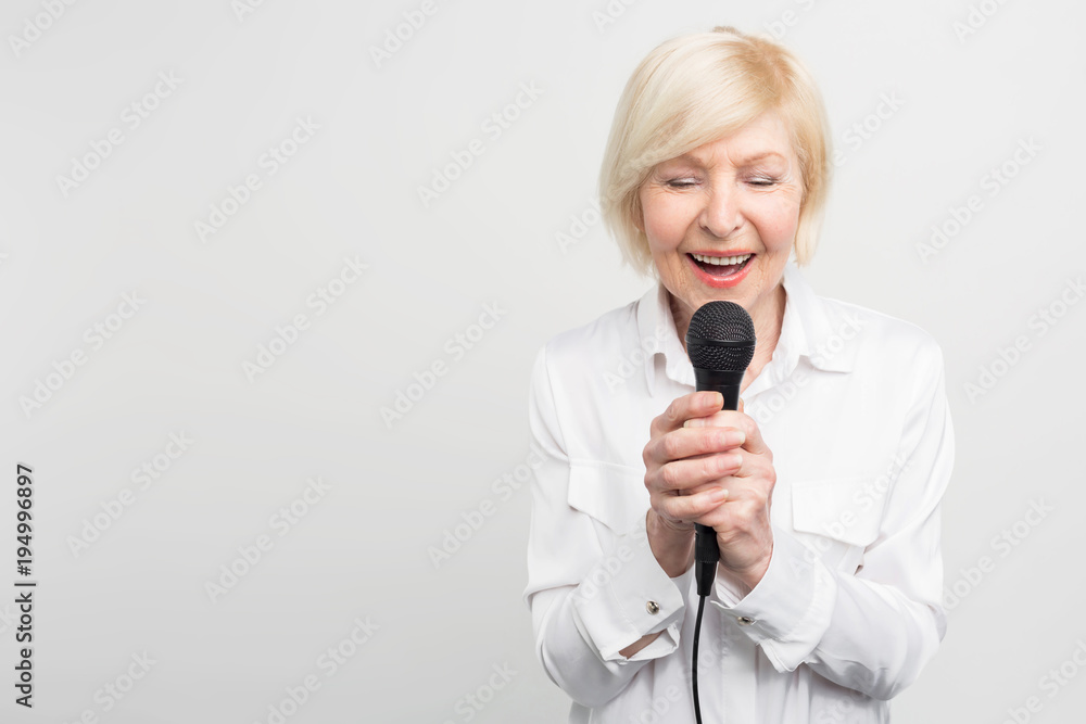 Beautiful and tender picture of awesome mature woman singing a song with her eyes closed using a microphone. Isolated on white background. Beautiful and tender picture of awesome mature woman singing a song with her eyes closed using a microphone. Isolated on white background.