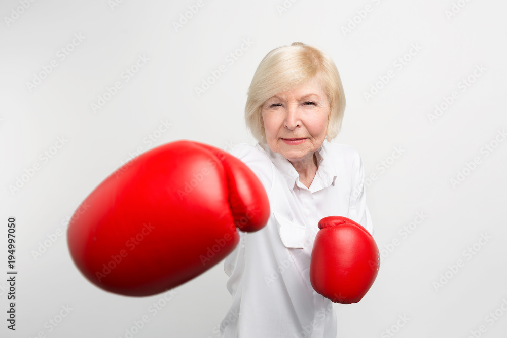 Serious woman is standing in position, wearing red boxing gloves. She is ready for doing some exercises. Isolated on white background. Serious woman is standing in position, wearing red boxing gloves. She is ready for doing some exercises. Isolated on white background.