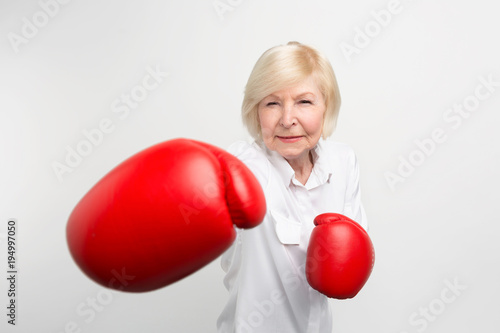 Serious woman is standing in position, wearing red boxing gloves. She is ready for doing some exercises. Isolated on white background.