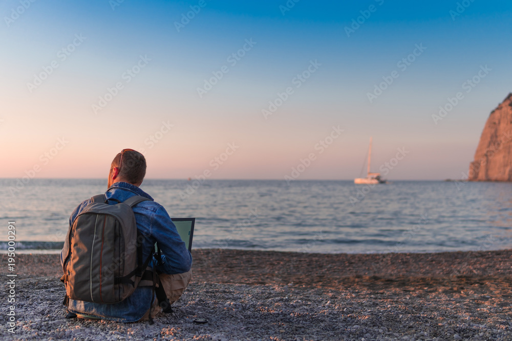 young man with laptop working on the beach. Freedom, remote work, freelancer, technology, internet, travel and vacation concepts