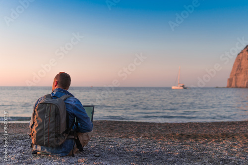 young man with laptop working on the beach. Freedom, remote work, freelancer, technology, internet, travel and vacation concepts © Sergey