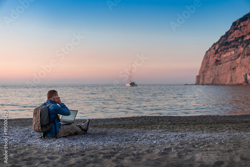 young man with laptop working on the beach. Freedom, remote work, freelancer, technology, internet, travel and vacation concepts