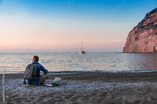 young man with laptop working on the beach. Freedom, remote work, freelancer, technology, internet, travel and vacation concepts