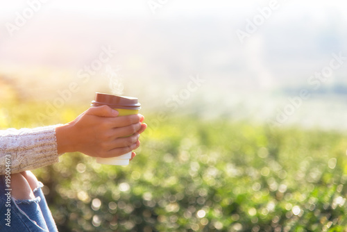 Hand women holding hot tea cup for drinking in the morning day, relaxing and sitting outdoor in the tea plantation in sunshine light enjoying life her warm at balcony. Lifestyle Concept