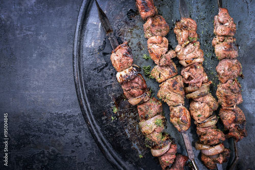 Traditional Russian shashlik on a barbecue skewer with roasted onion as top view on old board with copy space left photo