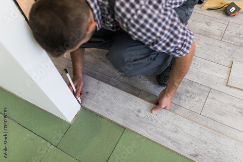 Male worker installing laminate flooring, man installing new wooden laminate flooring. Man laying laminate flooring at home. Carpenter worker installing laminate flooring in the room