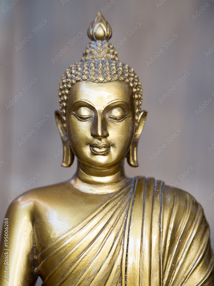 Golden antique buddha statue. The background is light slate gray. The face of the Buddha turned to the straight.