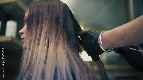 Hair stylist in black gloves is applying coloring dye on woman's hair to lighten up the hair tone in the beauty saloon. photo
