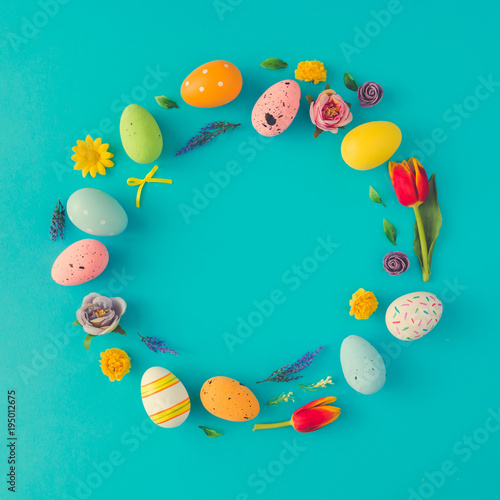 Creative Easter layout made of colorful eggs and flowers on blue background. Circle wreath flat lay concept.