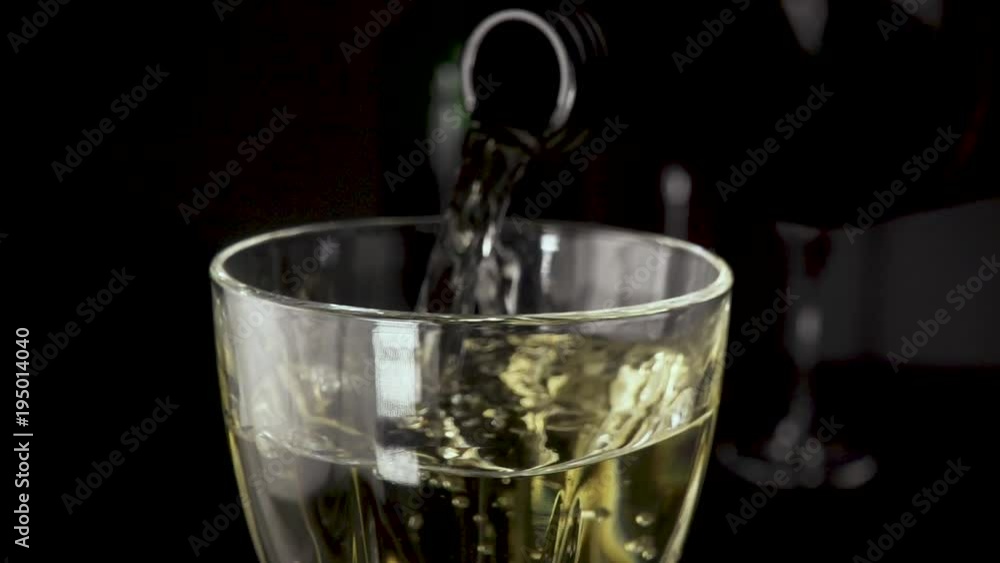White wine is pouring into a glass from a bottle the camera is moving to a close-up slow mo White wine is pouring into a glass from a bottle the camera is moving to a close-up slow mo