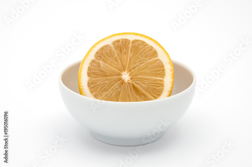 A half lemon in a white cup on a white background is isolated.