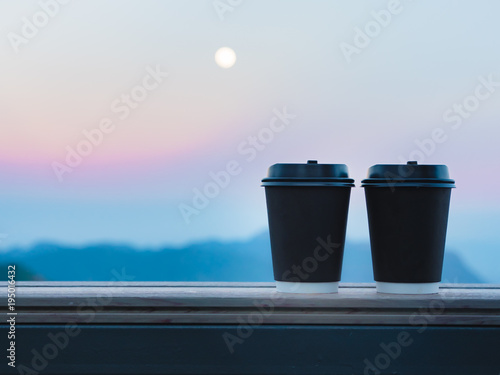 coffee break and relax concept from view from two black plastic coffee cup put on wooden table and layer of mountain with moon background