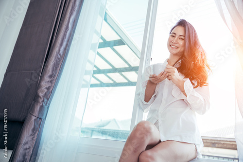 Asian girl who just wake up in the morning as relaxed. She opened the window to receive the light of the morning sun. She was holding a cup of coffee or tea to drink it. Free Download Asian girl who just wake up in the morning as relaxed. She opened the window to receive the light of the morning sun. She was holding a cup of coffee or tea to drink it. - GFXLoad