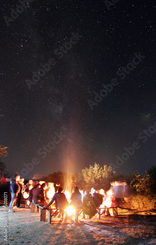 The people rest near a bonfire on the starry sky background. evening night time. long exposure