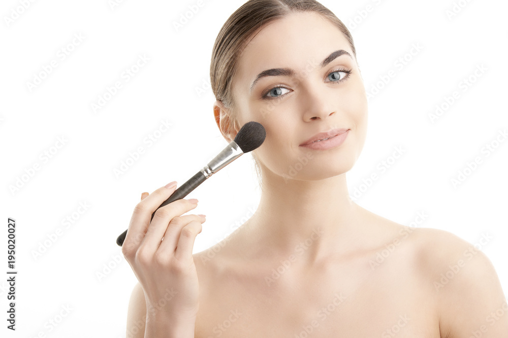 Close-up of a young woman holding brush in her hand and applying makeup. Isolated on light blue background. Close-up of a young woman holding brush in her hand and applying makeup. Isolated on light blue background.