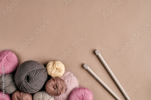 A group of colored balls of yarn and knitting needles on a beige background