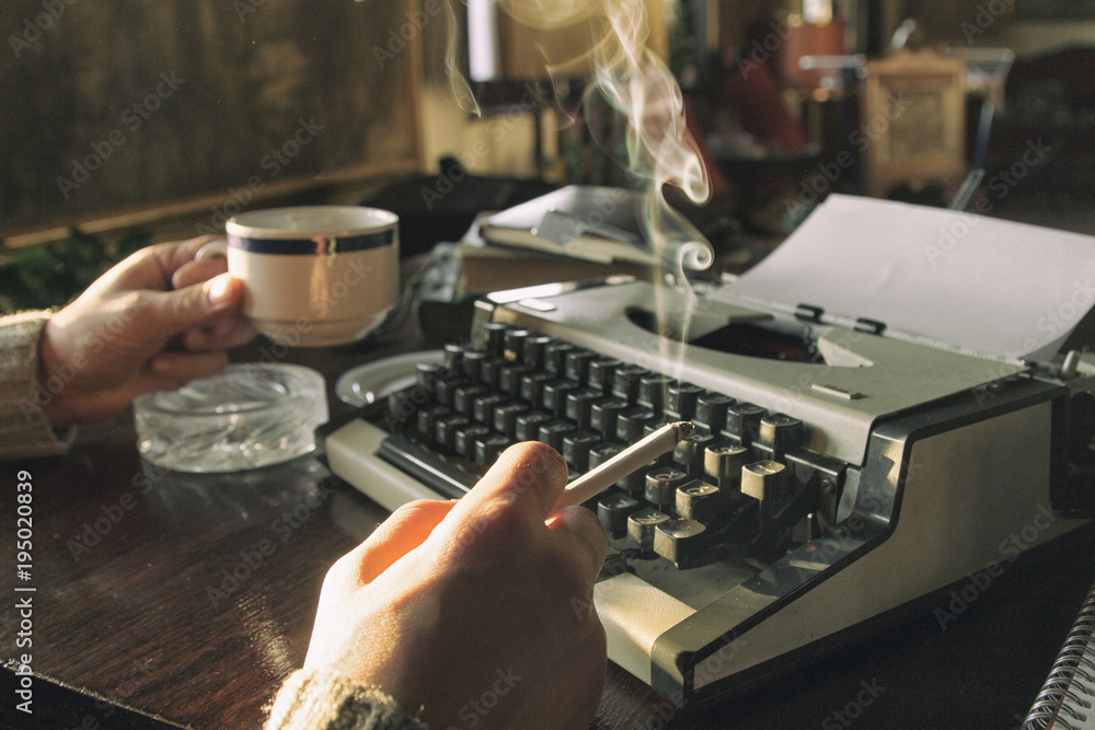 Handsome writer typing on old typewriter. smoking cigar and drinking coffee.