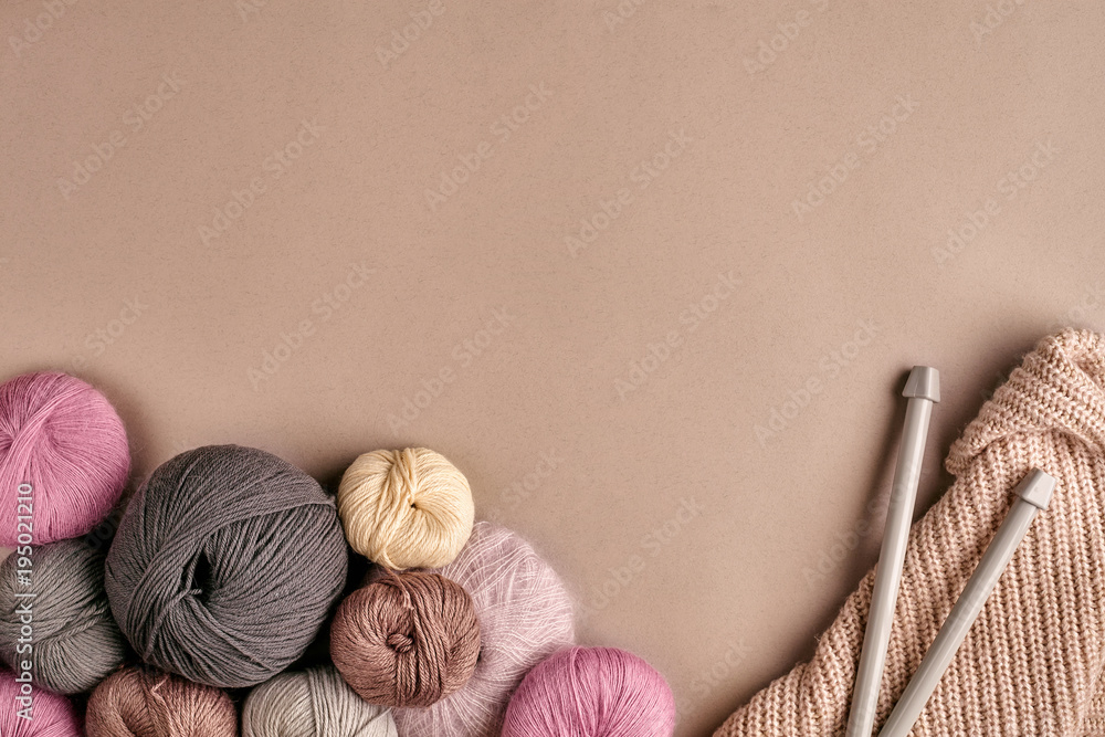 A group of colored balls of yarn and knitting needles on a beige background A group of colored balls of yarn and knitting needles on a beige background