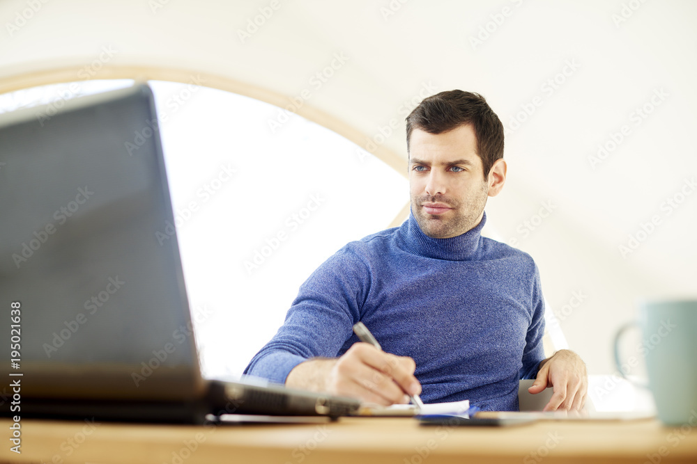 Young man working from home. Casual young man sitting in front of laptop and looking thoughtul while working. Home office. Young man working from home. Casual young man sitting in front of laptop and looking thoughtul while working. Home office.