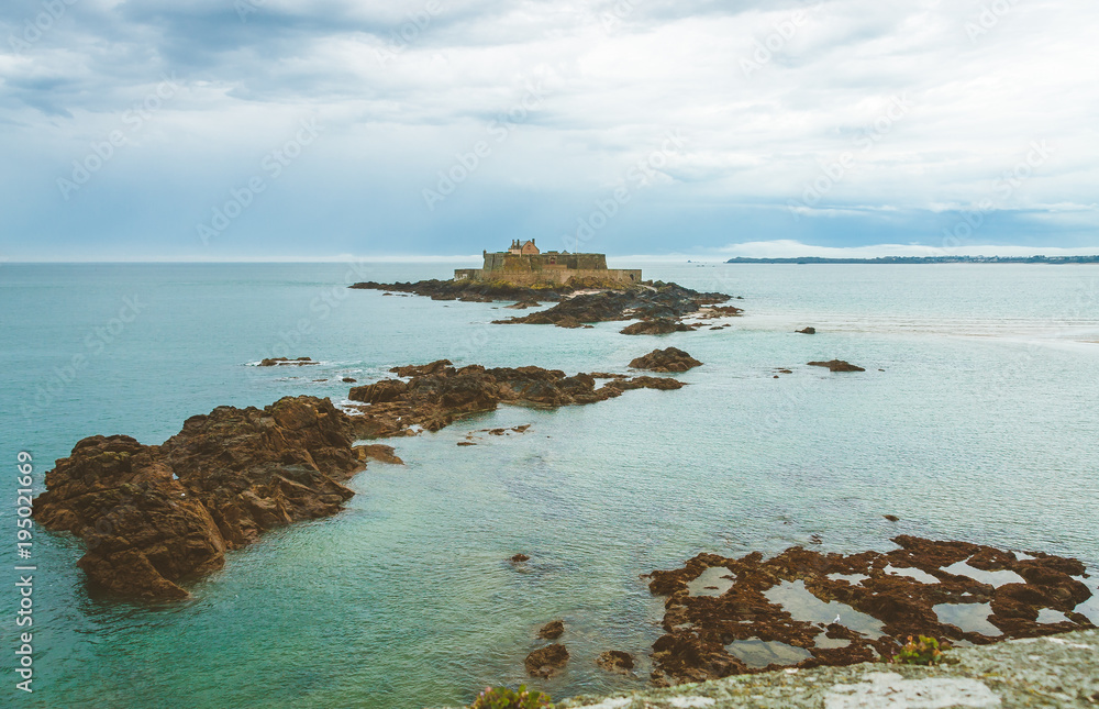 Fort National, ancient fortress on tidal island Petit Be and rocks in turquoise water on cloudy day in Saint-Malo, Brittany, France