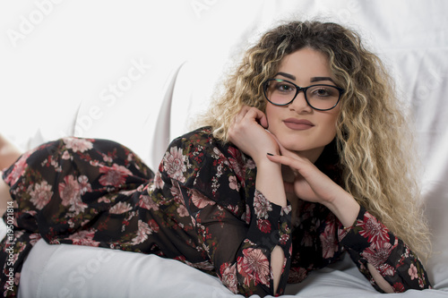 Woman with curly hair and floral dress posing on bed
