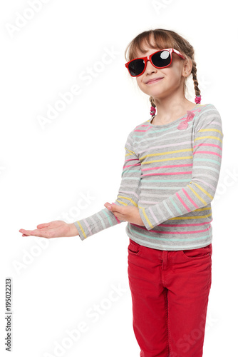 Child girl in sunglasses showing to side at blank copy space for your text or product, isolated on white background