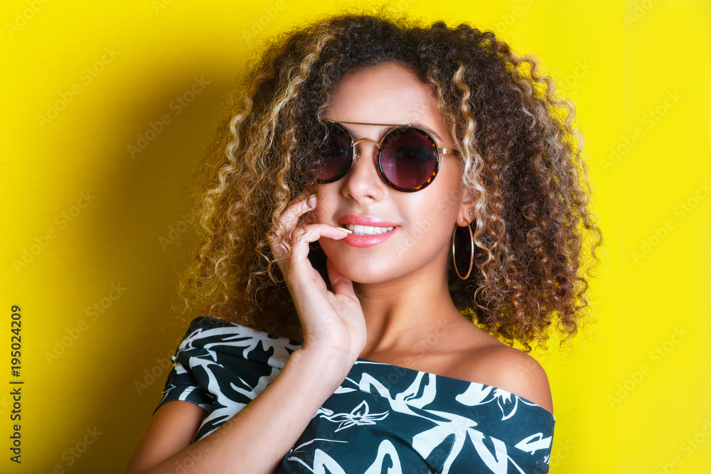 Fototapeta premium Beauty portrait of young african american girl with afro hairstyle. Girl posing on yellow background, looking at camera. Studio shot.