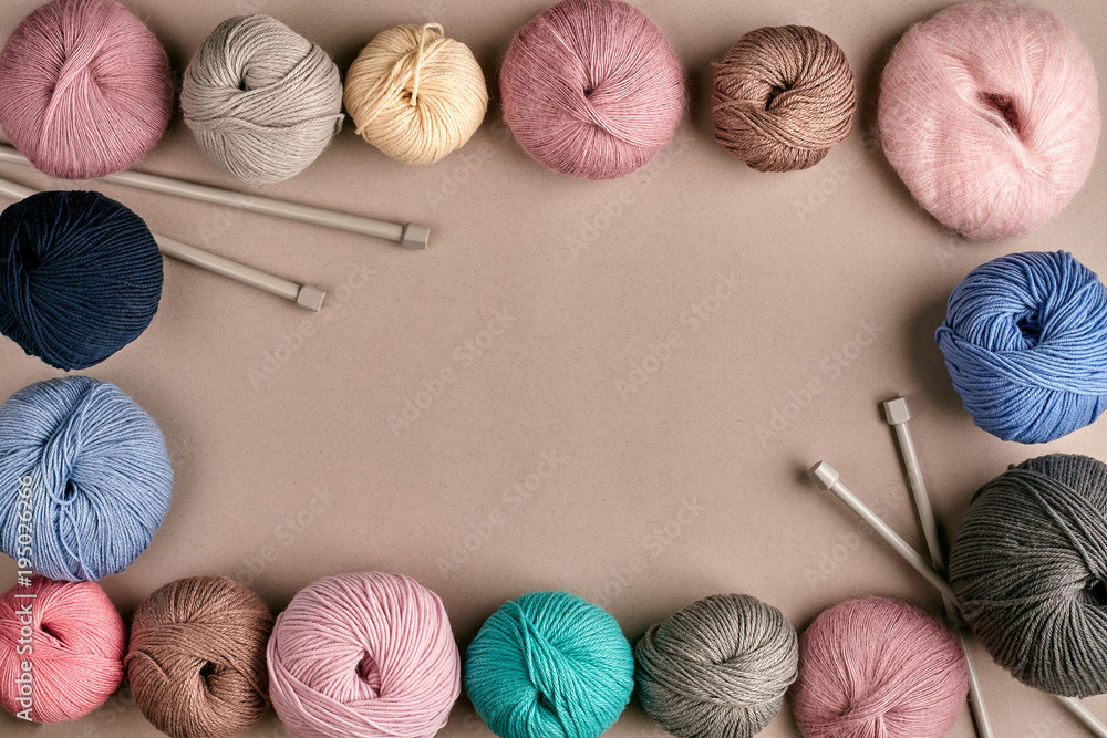 A group of colored balls of yarn and knitting needles on a beige background - obrazy, fototapety, plakaty 