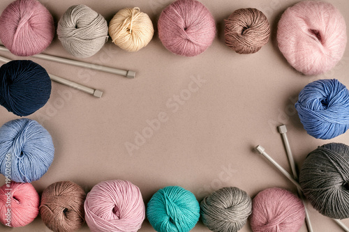 A group of colored balls of yarn and knitting needles on a beige background