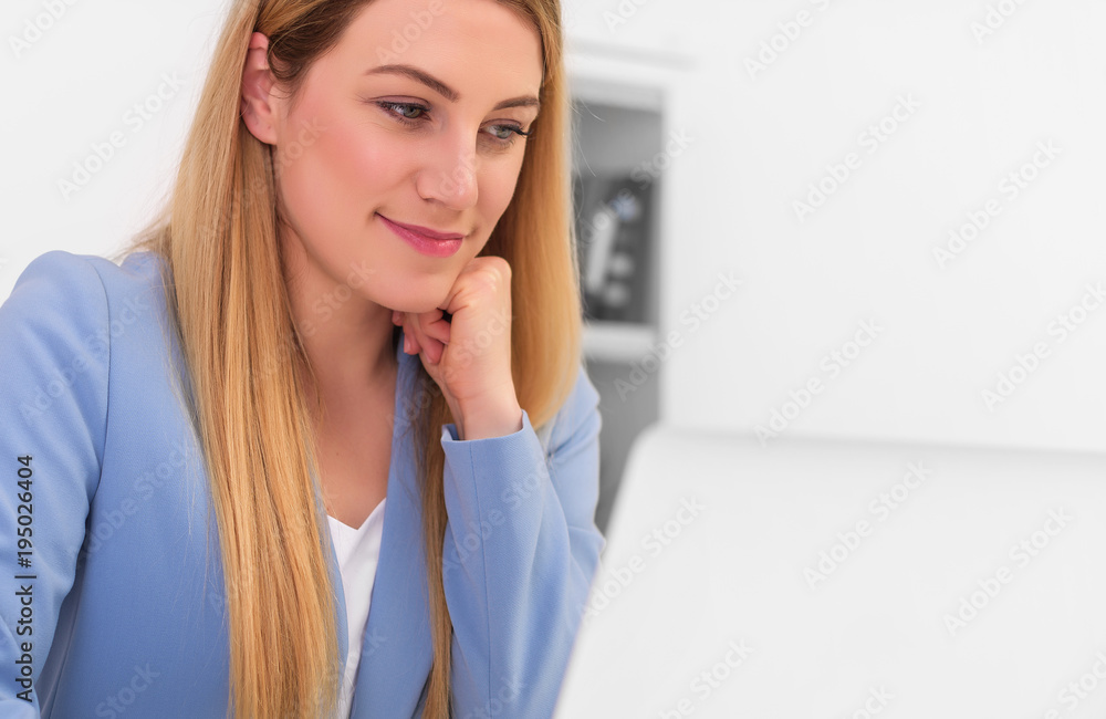 Beautiful young woman looks at the laptop monitor screen while sitting at the office desk. Beautiful young woman looks at the laptop monitor screen while sitting at the office desk.