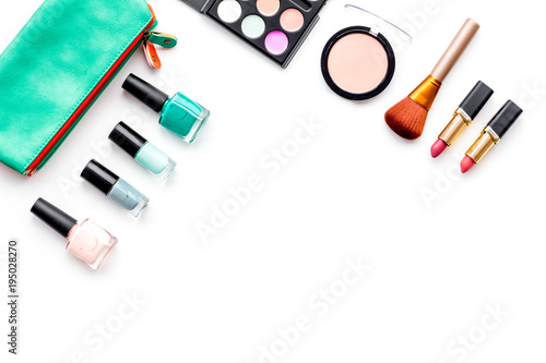 Makeup pattern. Eyeshadow, rouge, powder, brushes, lipstick, nail polish in cosmetic bag on white background top view copy space