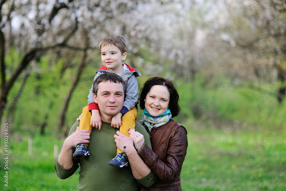 Young family - mom, dad and little son playing in the park against the background of spring green trees Young family - mom, dad and little son playing in the park against the background of spring green trees