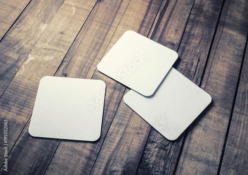 Blank white square beer coasters on wood table background.