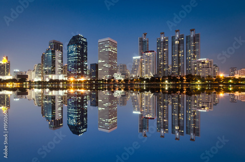 light from modern building bright in night city with skyline symmetric water mirror reflection. night cityscape concept. © thithawat