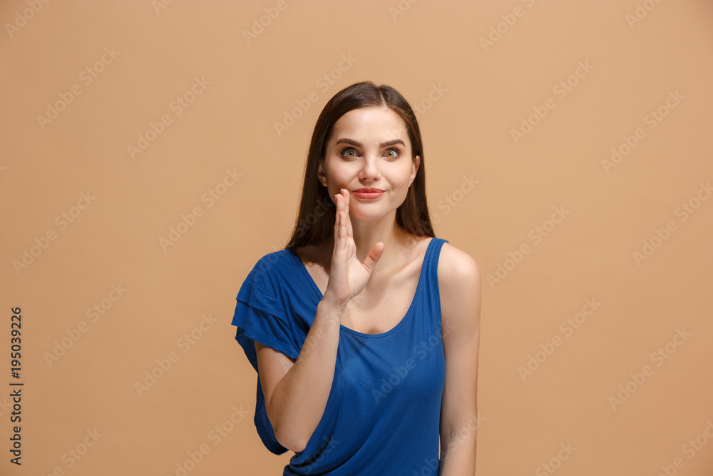 The young woman whispering a secret behind her hand over pastel background The young woman whispering a secret behind her hand over pastel background