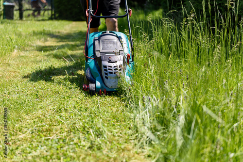 Man cutting grass with an electro lawnmower in his garden