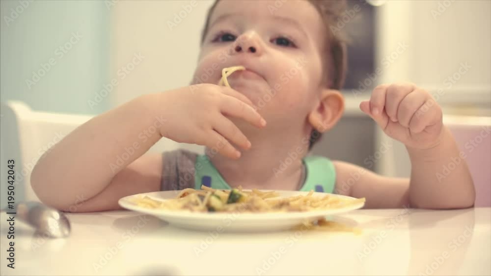 Small child is sitting at a table in a bib and eat his own spaghetti, the baby eats willingly. Small child is sitting at a table in a bib and eat his own spaghetti, the baby eats willingly.