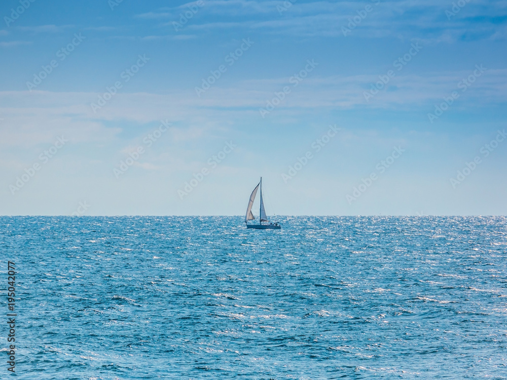 Sailing yacht with white sails in the open Sea. Blue water.