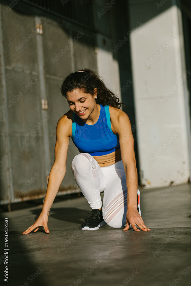 Fototapeta premium Cheerful female athlete getting ready for sprinting and running. Fit young sporty woman training outside.