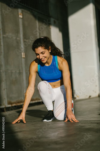 Cheerful female athlete getting ready for sprinting and running. Fit young sporty woman training outside.