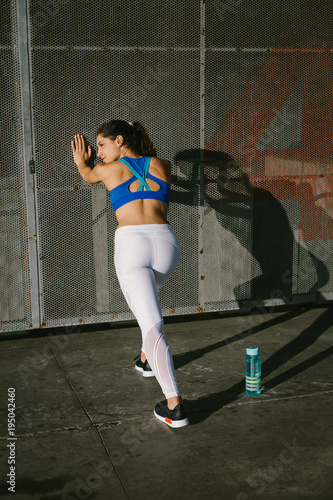 Fit female athlete stretching legs for warming up before urban running workout. Fitness young woman exercising outside. © Dirima