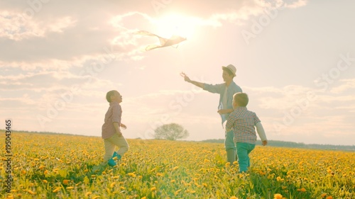 Little boys are playing flying kite with mother at sunset