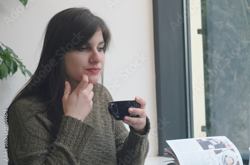 beautiful young woman drinking coffee near window