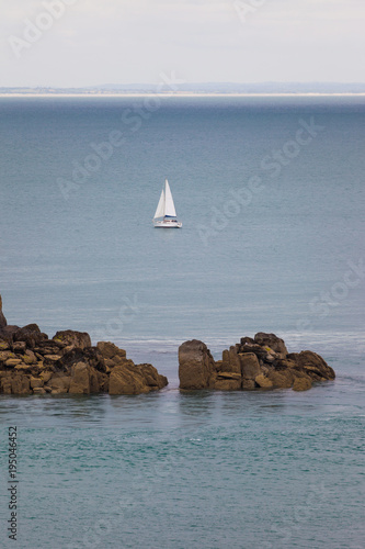 Sailboat with two sails behind the brown rock on ope waters of Bretagne coast. France photo