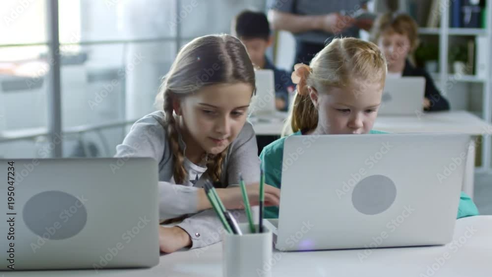 Two girls of primary school age doing task on laptop computer during information technology class, one helping another Two girls of primary school age doing task on laptop computer during information technology class, one helping another