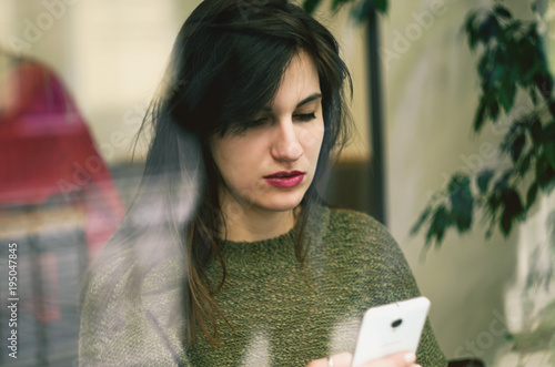 Cafe city lifestyle woman on phone texting text message on smartphone app sitting indoor in trendy urban cafe. Caucasian female model
