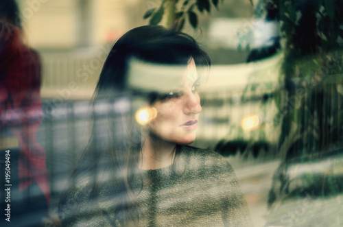 Young Girl waiting someone , and looking out behind the cafe window