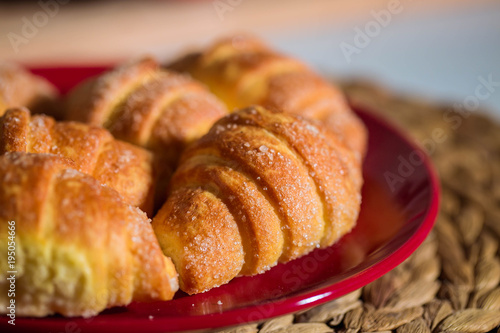 Homemade freshly baked croissants, sprinkled with sugar, on red plate. Closeup