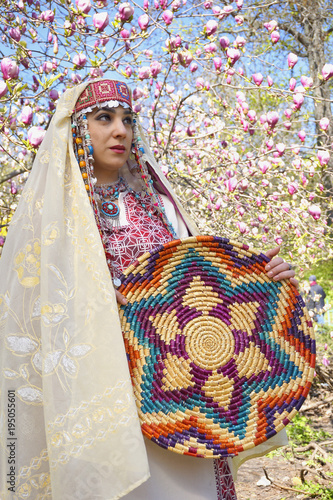 Girl against of magnolia flowers in national Palestinian costume, with head covered. 
