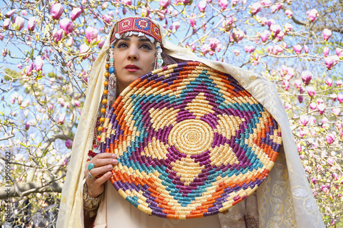 Girl against of magnolia flowers in national Palestinian costume, with head covered. 